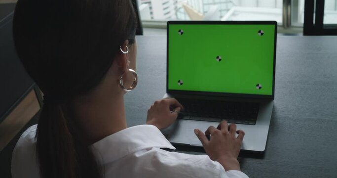 Over shoulder view freelancer sitting on chair working business ideas using laptop with green screen computer with mock up chroma key display. Female freelancer searching the network use isolated pc