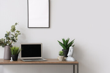 Modern laptop and different houseplants on table near white wall