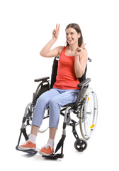 Young woman in wheelchair showing victory gesture on white background