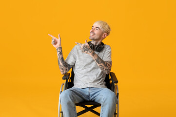 Young tattooed man in wheelchair pointing at something on yellow background