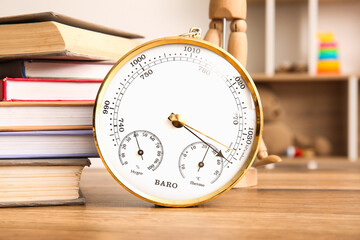 Aneroid barometer and books on wooden table in room, closeup