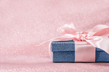 Blue sparkling gift box with pink ribbon bow on pink bokeh background. Gift or holiday concept. Mothers Day, birthday wedding or St Valentines day with copy space. Minimal monochrome wide banner