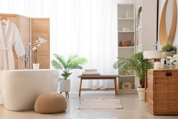 Interior of light bathroom with grey bench and bathtub