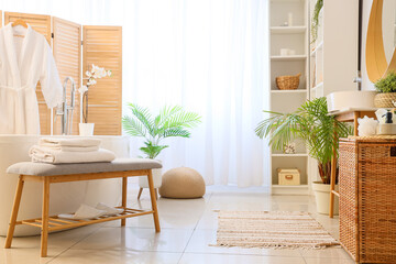 Interior of light bathroom with grey bench and bathtub
