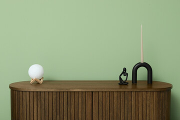 Modern brown chest of drawers with candle and moon lamp near green wall in room