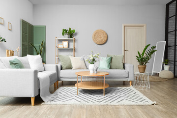 Interior of modern living room with grey sofas, flower vase on coffee table and houseplants