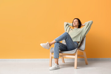 Beautiful young woman resting in comfortable chair near yellow wall