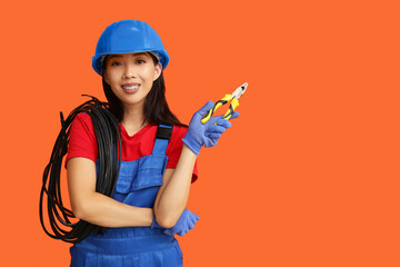 Young female electrician with pliers and cables on orange background