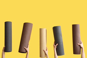 Female hands with yoga mats on yellow background
