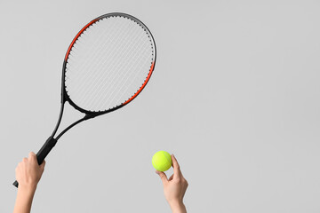 Female hands with racket and tennis ball on grey background