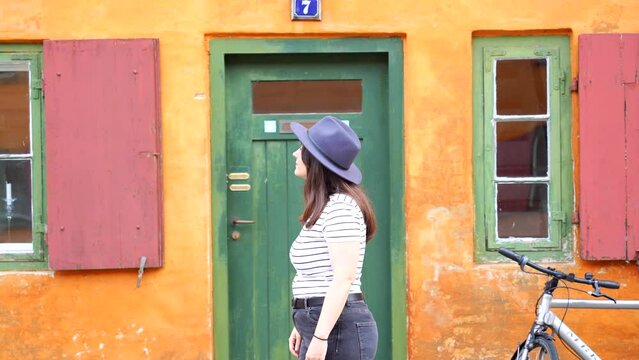 Caucasian woman fixing her hat in front of yellow house in Nyboder, Copenhagen