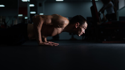 Muscular shirtless man doing push ups in the gym.  - obrazy, fototapety, plakaty