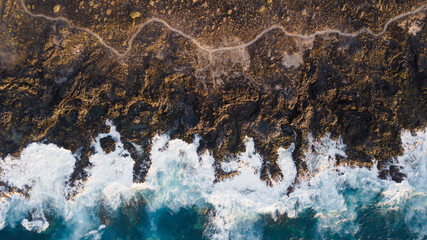 Drone view of Tenerife south coast with Atlantic ocean and strong swell beating against the walls of a rocky cliff, blue rough sea with big waves with foam crashing against the rocks - Powered by Adobe