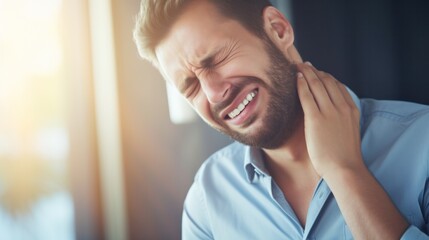 A man grimacing in pain, holding his neck with one hand, indicating discomfort and possible neck pain. - obrazy, fototapety, plakaty