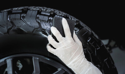 Professional car service worker polishing car tires with black sponge