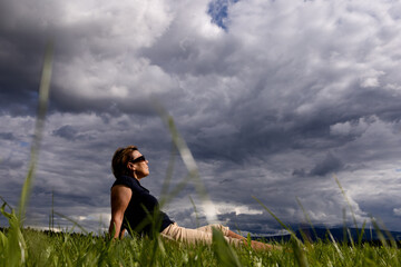 Fototapeta na wymiar A tourist is resting on a field under dark low clouds
