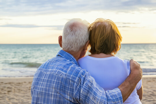 an elderly couple is relaxing at sea. grandparents sit in an embrace with their backs to the camera and look at the sea. happiness and long life concept
