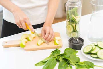 Vegetable smoothie detox, woman hand making healthy raw fresh green fruit juice with blender machine, preparing drink with spinach in kitchen at home, eating vegan diet. Healthy dieting, weight loss.