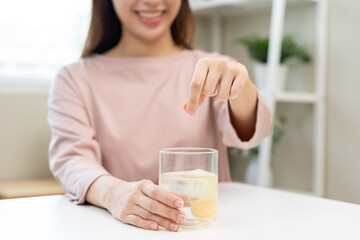 Smile asian young woman putting or dropping effervescent tablet into glass of water, holding pain pill, painkiller medicine, aspirin for treatment, take vitamin c for hangover. Health care concept.