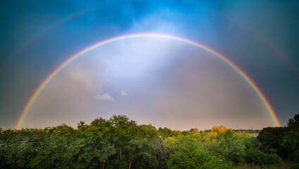 Tranquil scene with double rainbow in colorful sky over forest