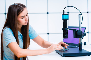 young female laboratory assistant uses a microscope to control electronic devices PCB