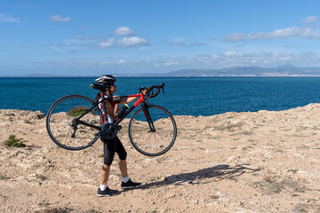 Obraz premium Woman cyclist carrying her bicycle along a broken path in front of the sea. Concept of sporty, active, happy woman