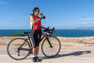 Fototapeta premium Cyclist woman drinking water next to her bicycle. Concept of sporty, active, happy woman