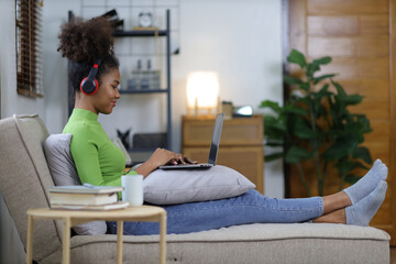 Attractive young african woman sitting on sofa using laptop leisurely and relaxing in living room at home.