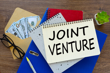 JOINT VENTURE text on a notepad on a blue folder. money in an envelope