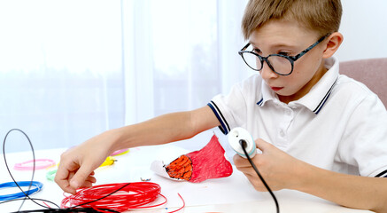 a boy plays with a 3D pen at the table