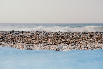 Blue yoga mat is on a sandy pebble beach by the sea. Nobody. Women's yoga fitness routine. Healthy lifestyle, harmony