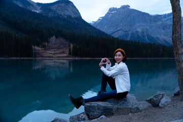 Portrait of woman traveler making heart hands while sitting at Emerald Lake, Alberta, Canada. Tourist feel happiness, freshness, life, energy, enjoy, cheerful, relax, outdoor, cold, roadtrip