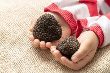 a young boy holding two black truffles in his hands
