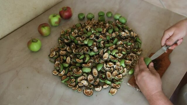 Man peeling and eating walnuts in green husks at kitchen table. Close-up of hands, top view.