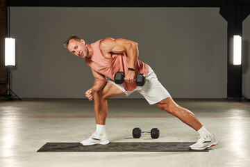 one-arm dumbbell row in a bent-over position with emphasis on the leg by a handsome Caucasian...