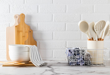 A set of kitchen utensils on a light stone countertop against a white brick wall. Kitchen textiles....
