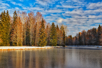 Landscape of the picturesque nature of the park, colorful trees, a frozen river and the first snow in late autumn