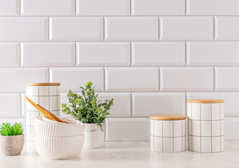 Fototapeta na wymiar Set of stylish white ceramic jars with bamboo lids and white ceramic bowls on white stone countertop. Trendy eco style in a modern kitchen.