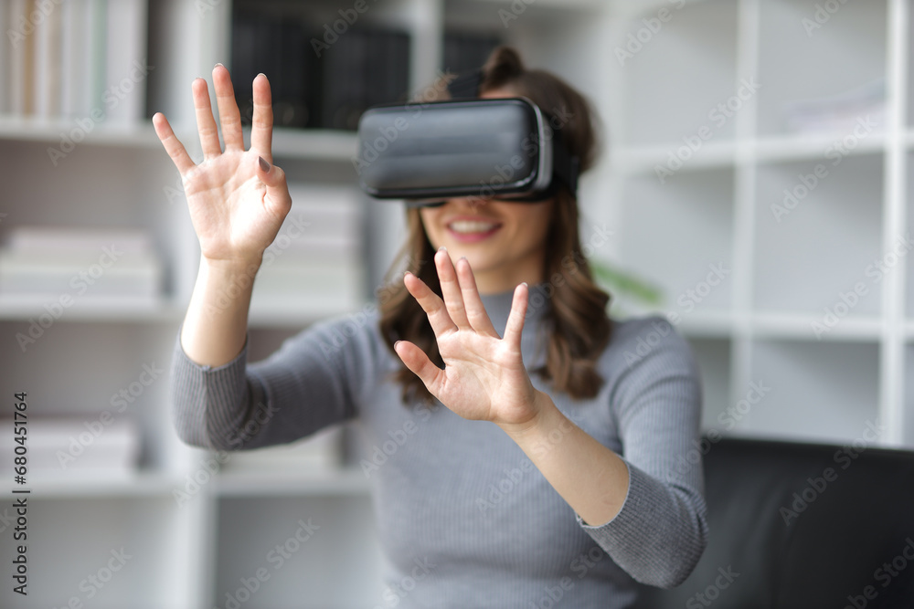 Wall mural a woman sitting on a sofa in the living room wearing vr 3d glasses looks excited about a movie.