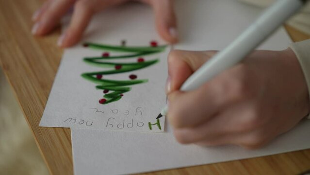 A left-handed woman signs a handmade New Year's card with a green felt-tip pen