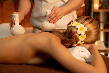 Closeup hot herbal ball spa massage body treatment, masseur gently compress herb bag on woman body....
