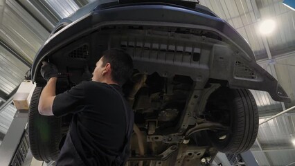 An auto mechanic working under the car on a car lift in the garage, he disassembles the bottom of the car for further repair. Antifreeze drain in the service station. Auto repair shop, auto repair.