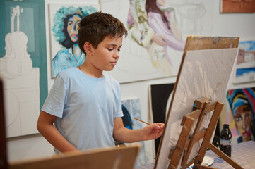 Authentic portrait of Caucasian elementary age school boy drawing picture on canvas at art class in creativity workshop