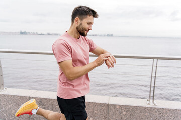 Uses a fitness app in a smartwatch, a male runner. A fitness trainer trains alone in sportswear.