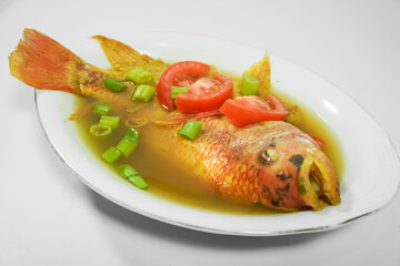 Tilapia fish soup in a bowl with turmeric sauce and spices, using sliced tomatoes and spring onions as garnish - Isolated on white backgrounds. Concept for whole healthy food, omega-3, animal protein.