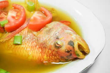 Tilapia fish soup in a bowl with turmeric sauce and spices, using sliced tomatoes and spring onions as garnish - Isolated on white backgrounds. Concept for whole healthy food, omega-3, animal protein.