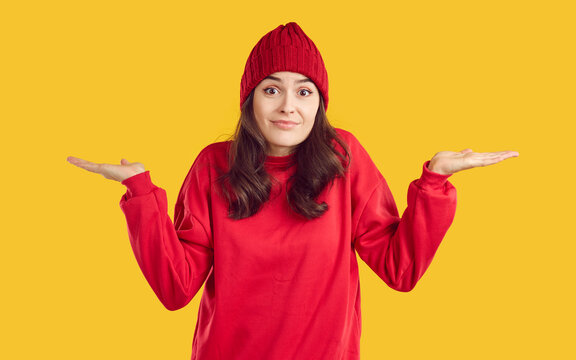 No idea. I'm clueless. Sorry, can't help you. There's nothing I can do. Pretty brunette woman in red sweatshirt and autumn hat looks at camera and shrugs shoulders isolated on yellow studio background