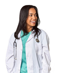 Young Filipina doctor with stethoscope in studio looks aside smiling, cheerful and pleasant.