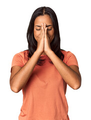 Young Filipina with long black hair in studio holding hands in pray near mouth, feels confident.