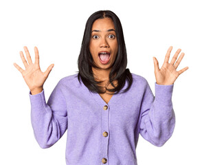 Young Filipina with long black hair in studio receiving a pleasant surprise, excited and raising hands.